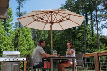 Couple dining under Alizé Antigua 10ft market umbrella showing full coverage over outdoor patio table versus smaller 9ft umbrella