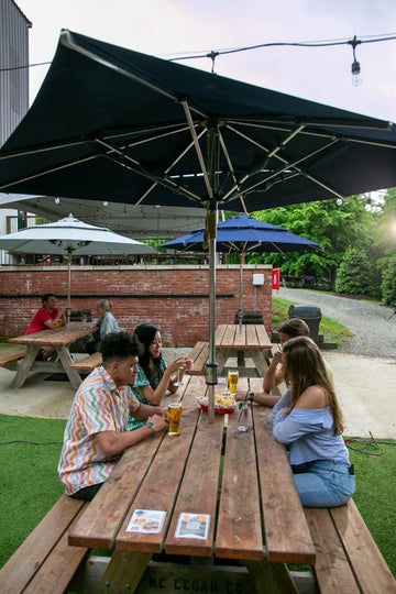 Guests dining at outdoor restaurant patio table under market umbrella  on hot summer day showing need for built-in cooling fans