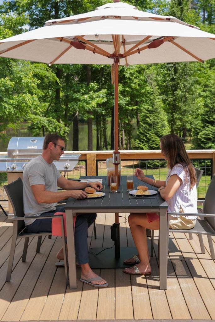 Couple dining outdoors under Alizé Antigua 10ft market umbrella with built-in fans on wooden deck surrounded by trees