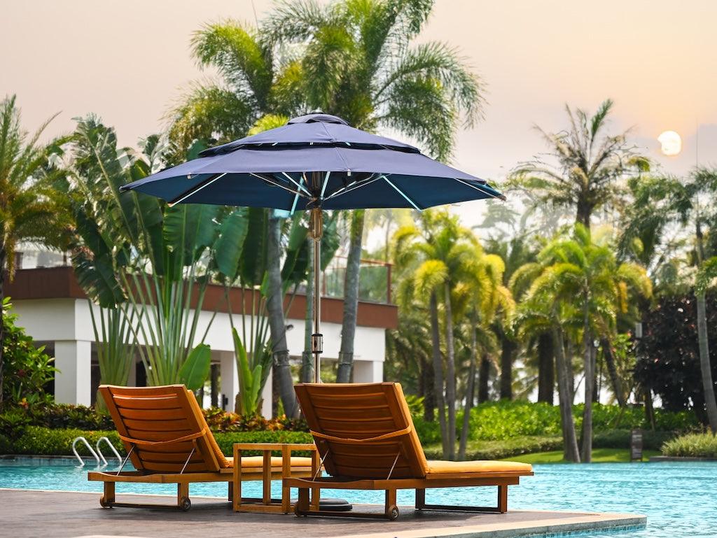 Alizé St. Martin 9ft navy market umbrella with built-in fans over two lounge chairs beside tropical resort pool at sunset